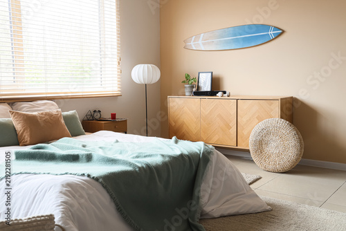 Interior of bedroom with bed, surfboard and sound speaker on commode