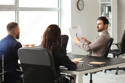 Male court mediator with clipboard and people working at table in office