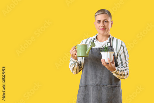 Female gardener with plant and watering can on yellow background