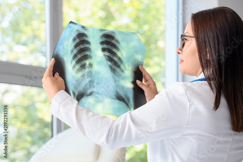 Female doctor studying x-ray image of lungs in clinic, back view