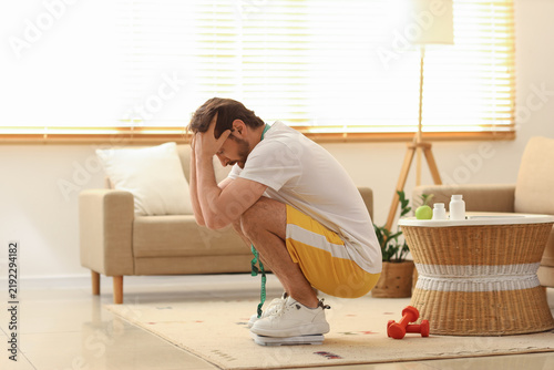 Stressed young man measuring weight on scales at home