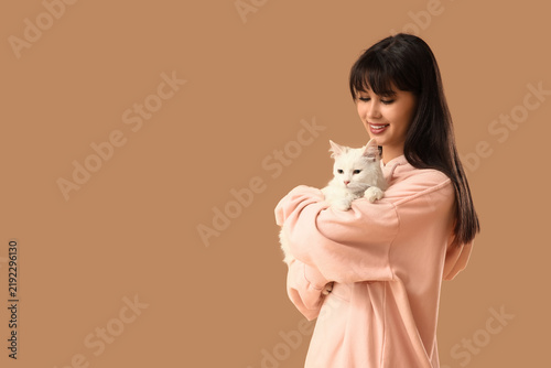 Beautiful young happy woman with cute white cat on brown background