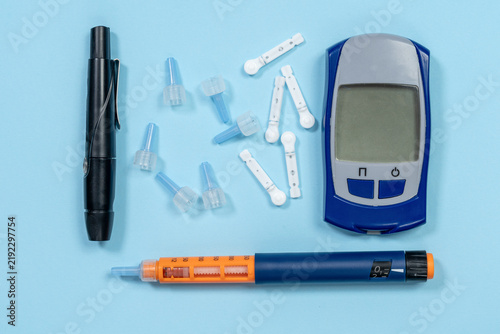 Fotografía A blood glucose meter, lancing device, insulin pen, and scattered lancets are arranged flat on a blue background, a concept of diabetes care and blood sugar monitoring at home
