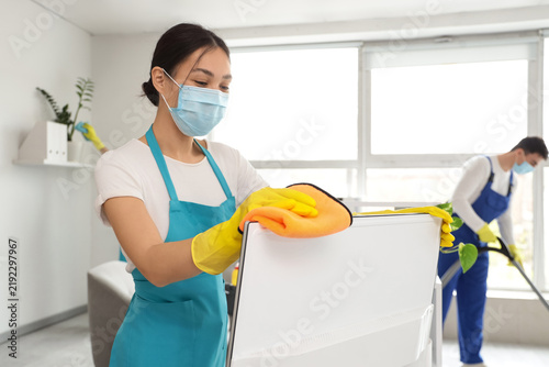 Female Asian janitor with mask cleaning computer monitor in office