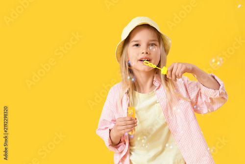 Little girl blowing soap bubbles on yellow background