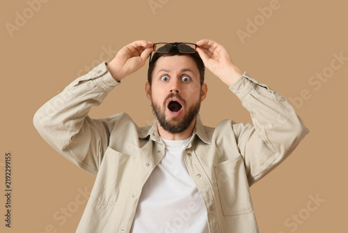 Surprised young man with eyeglasses on beige background