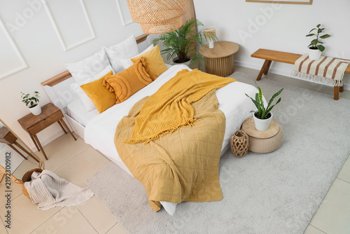Interior of light bedroom with big bed, tables and plants