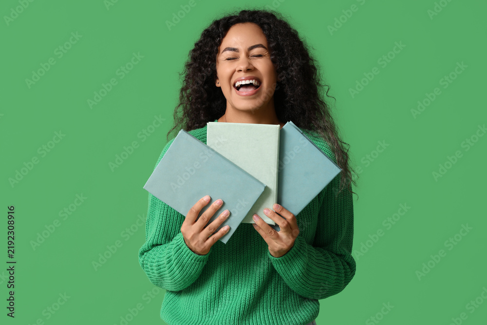 Fototapeta premium Happy young African-American woman with books on green background