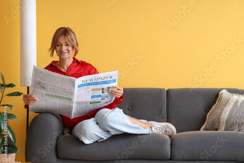 Pretty young woman reading newspaper on sofa at home