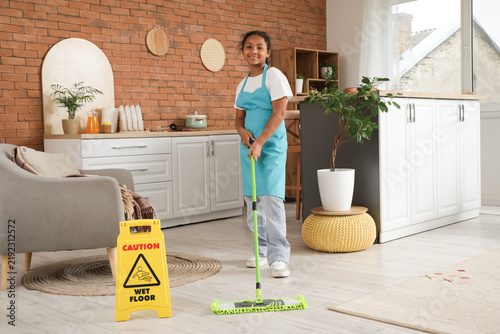 Teenage African-American janitor with caution sign mopping floor at home