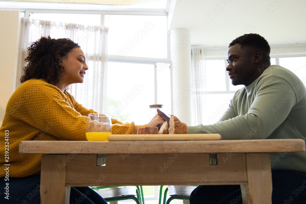 Fototapeta premium African American couple sitting at table holding hands in mustard sweater and green top with bread