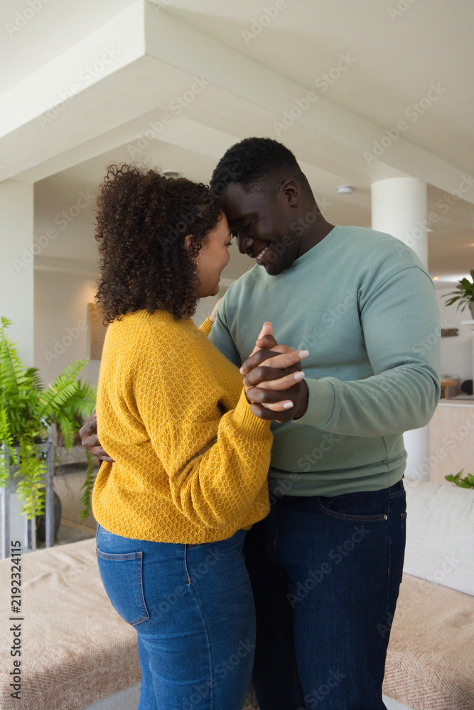 Obraz premium African American couple holding hands swaying at home near sofa wearing mustard knit and green top