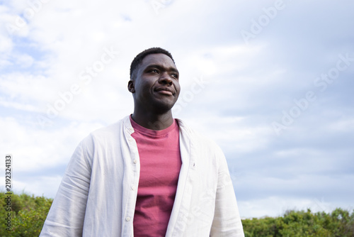 African American adult male standing looking up right in field wearing maroon tee and light shirt
