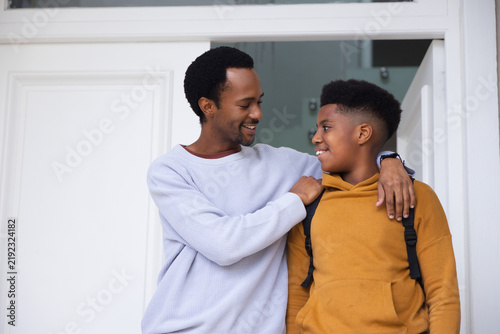 African American father and teenage son standing at entry, smiling, wearing sweater hoodie backpack