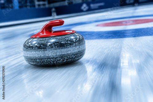 Granite curling stone sliding down an ice sheet towards the target, motion blur.