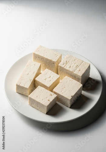 A white plate holds seven rectangular blocks of tofu. The tofu pieces are arranged in a slightly haphazard manner.