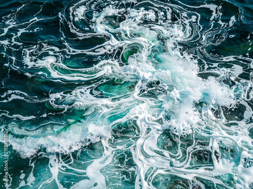 Abstract texture of white foam swirling on dark blue-green water surfa