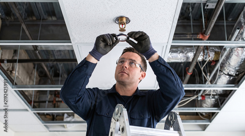 Fire safety technician installing an escutcheon ring on a ceiling sprinkler head