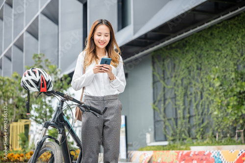 Fotografie In the city a cheerful woman on her bike remains connected through her smartphone