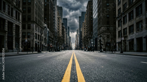 Empty city street with double yellow lines stretching through a downtown urban canyon under moody sky