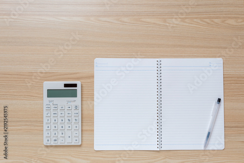 Calculator, pen and blank notebook on wooden desk for budgeting and financial planning