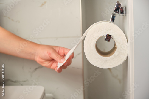 Hygiene and personal care hand pulling toilet paper from a roll in a bathroom for daily sanitation and household maintenance in a modern home