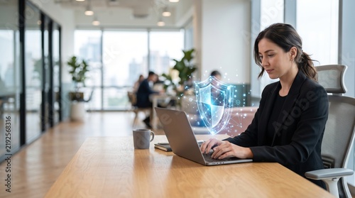Businesswoman using laptop with digital shield overlay for cybersecurity concept