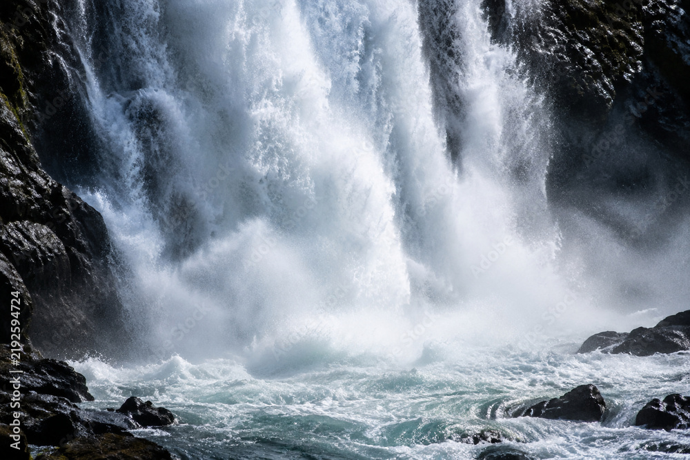 Obraz premium Powerful waterfall crashing into rocky pool, symbolizing raw natural force and strength
