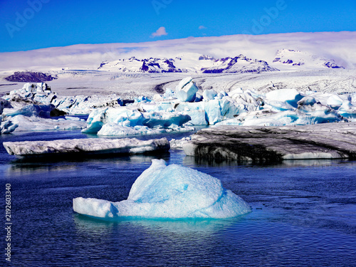Fotografía A floating blue iceberg drifts in the foreground across Jökulsárlón glacial lago