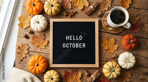 Cozy autumn flat lay with mini pumpkins, coffee, and a sign saying hello october on a wooden table