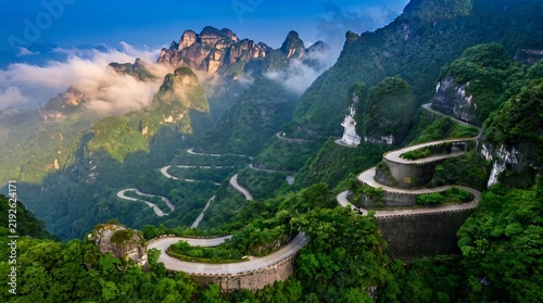 Curving mountain road winds through lush green forest with scenic cliffside views for travel marketing or Dramatic winding road through dense forest and rocky cliffs, ideal for tourism and automotive.