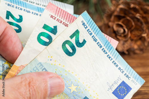 Canvastavla Close-up of a hand holding Euro banknotes on a wooden background with a pine cone
