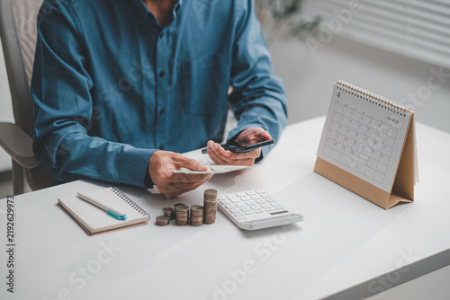 Konstfotografi Businessman holding banknotes and smartphone beside desk calendar, calculator, a