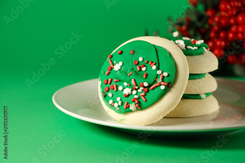 Frosted sugar cookies on a white plate with some berries in the background
