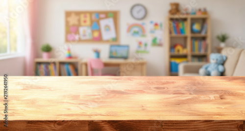 Empty wooden tabletop fronts child learning space, with bookshelves, desk, wall art, and teddy bear in soft blur. Bright classroom style room suggests child study area and playful learning mood.
