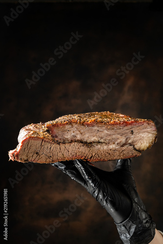 sliced smoked beef brisket with seasoned bark and smoke ring. Barbecue meat on dark rustic background.