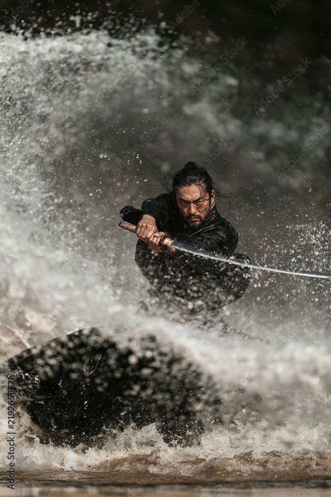Fototapeta premium Man with sword stands in water while splashing waves around him during a dynamic action scene