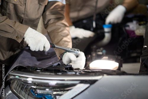 Mechanic hands wearing white gloves using a wrench to fix a car engine