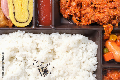 Korean lunch box with rice, meat, and kimchi in plastic packaging close-up, top view.