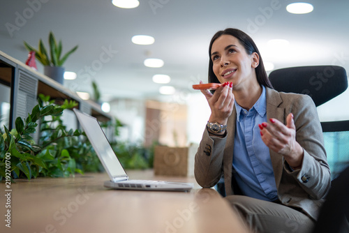 Foto Businesswoman using a smartphone speakerphone while working at her desk