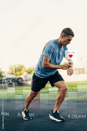 Fotografie Runner checks heart rate during training session in a park on sunny day
