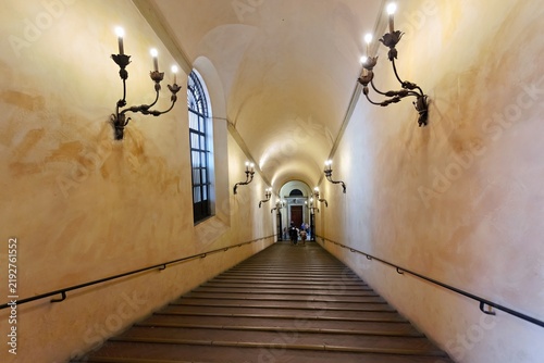 View of the long covered staircase of the Portico di San Luca with arched ceilings, wall-mounted lamps, and handrails in Bologna, Emilia-Romagna, Italy.