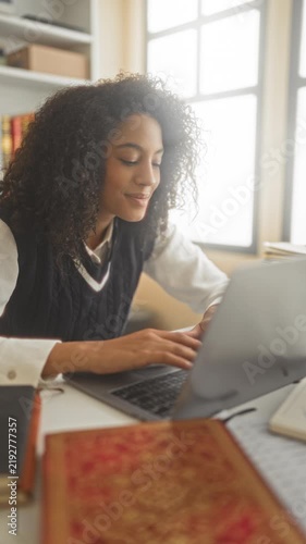 Young woman student typing on laptop with hands on keyboard at a desk in building, books and notebook nearby; concentration learning.