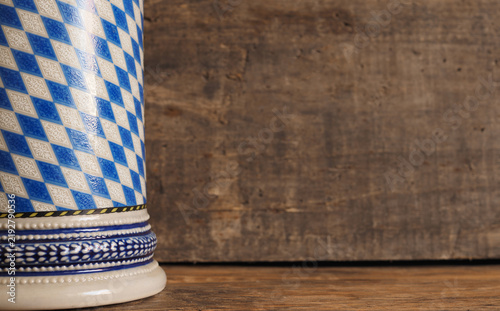 A Bavarian beer mug with a bavarian flag in front of a wooden background with space for text