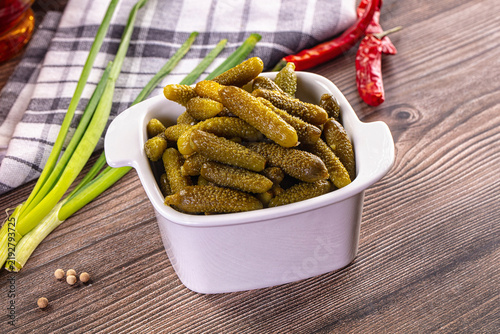 фотографія Pickled gherkins in white ceramic bowl on rustic wooden table with green onions