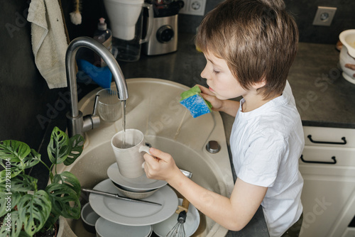 Boy washing dishes in kitchen sink doing chores