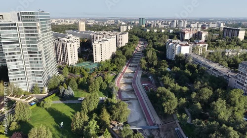 Drone view flying along city river channel with apartment buildings and walking promenade