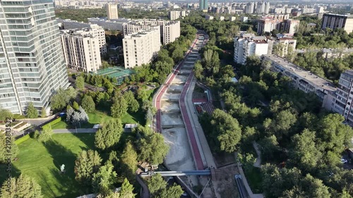 Drone view flying along city river channel with apartment buildings and walking promenade