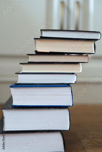Bild auf Leinwand Tall stack of closed hardcover books forms an uneven column on a table