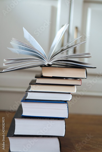 Cuadro en lienzo Open book with fanned pages balances on a leaning stack of hardcover books